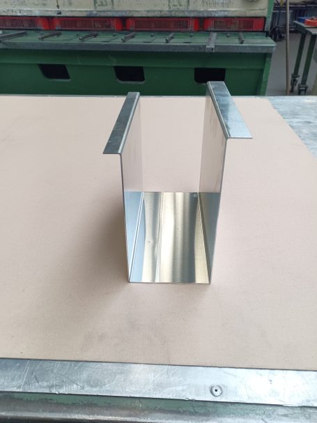 Ein glänzendes, rechteckiges Metallstück mit offenen Kanten, stehend auf einem Tisch.